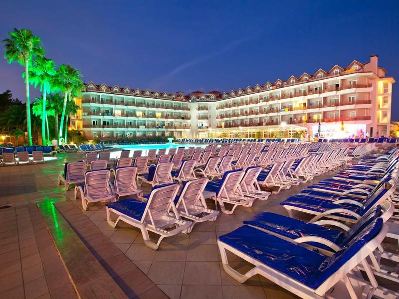 Hotel with rows of lounge chairs in front of the building at night with green lighting and a blue sky.