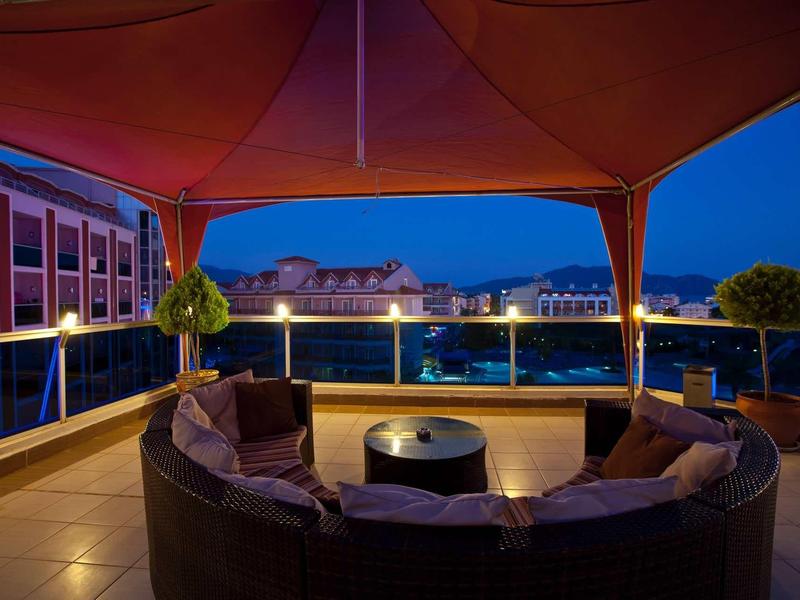 Cozy terrace with seating and view of illuminated city and mountains at night.
