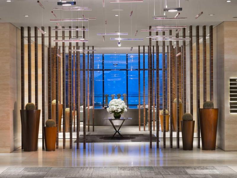 Moderní hotelová hala s velkými vázy a výhledem na moře při západu slunce.