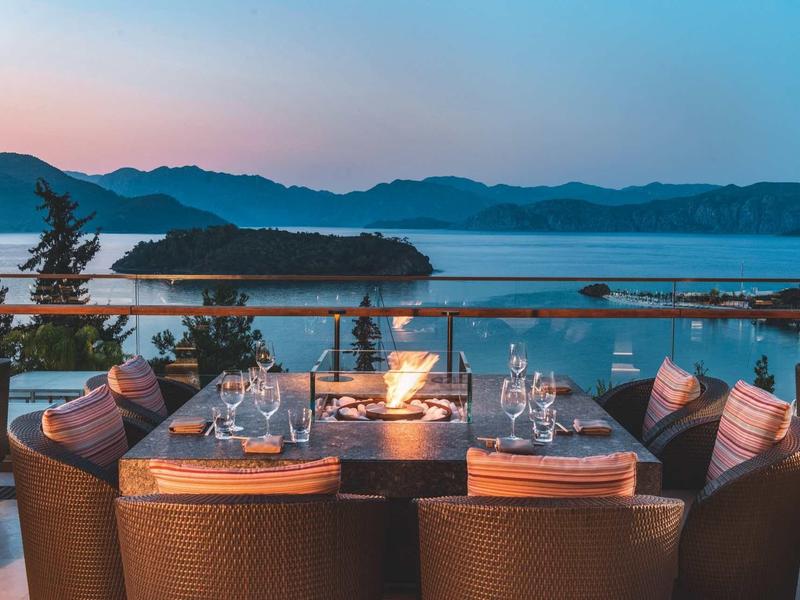 Hotelová terasa s prostřeným stolem a výhledem na jezero a hory za soumraku.