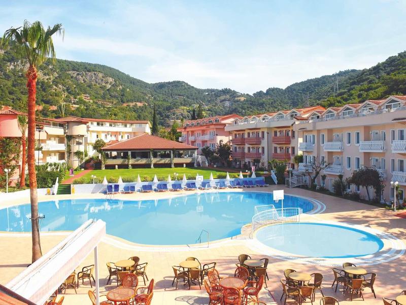Groot buitenzwembad in een hotelcomplex omgeven door meerlaagse gebouwen en bergen op de achtergrond.