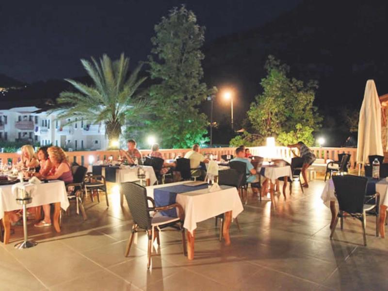 Buitendiner met gedekte tafels en gasten in een verlichte ruimte met palmbomen 's avonds.