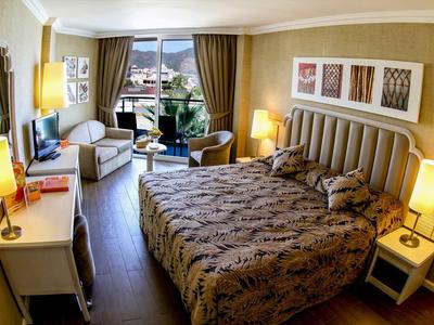 Camera d'hotel con letto grande, poltrone, scrivania e vista mare da finestre a tutta altezza.