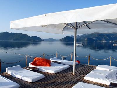 Rustruimte met ligbedden en parasol op houten terras met uitzicht op rustig meer en bergen.