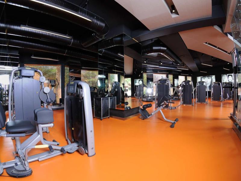 Ampia palestra con pavimento arancione e varie attrezzature per forza e cardio.