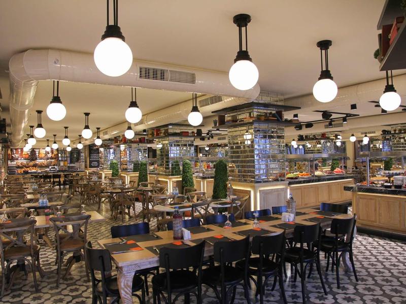 Ristorante moderno con molti tavoli, sedie e lampade rotonde al soffitto.