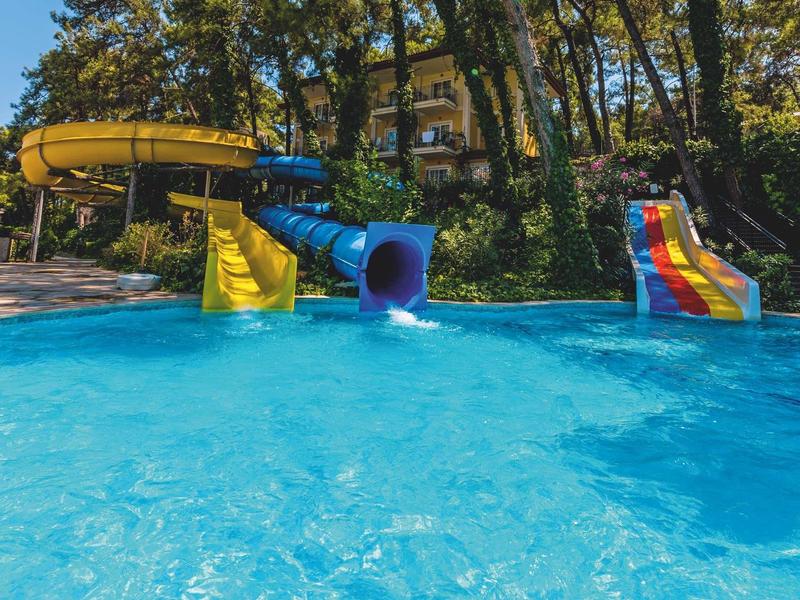 Wasserpark mit zwei Wasserrutschen, klarem Pool und Bäumen im Hintergrund.