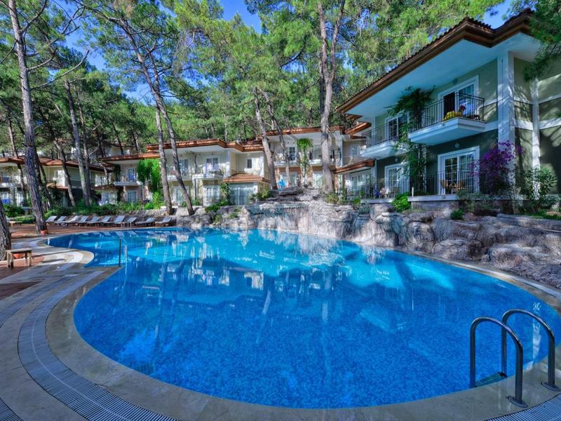 Ein blauer Pool umgeben von Bäumen und mehrstöckigen Gebäuden im Sonnenlicht.