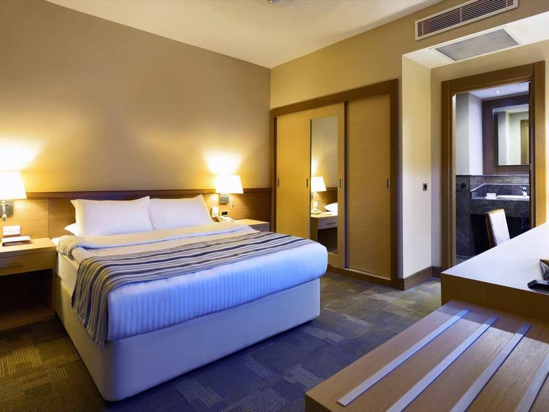 Modern eingerichtetes Schlafzimmer mit großem Bett, Wandlampen, Spiegel und Holzregalen.