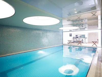 Modern indoor pool with round ceiling lights and glass wall to lounge