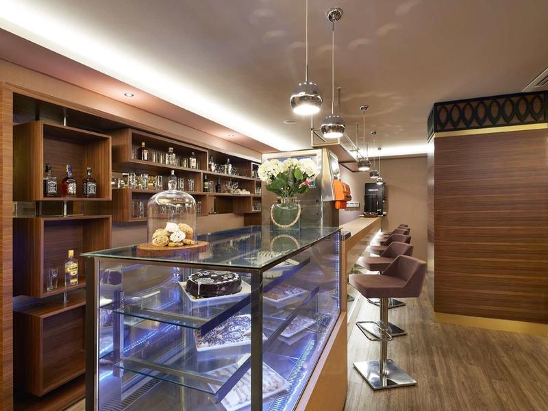 Modern hotel lobby with glass display case, sleek counter, and wooden bar stools.