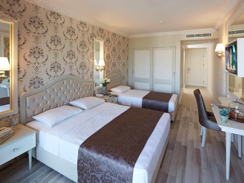 Bright hotel room with two beds, desk, TV, and elegant wallpaper.