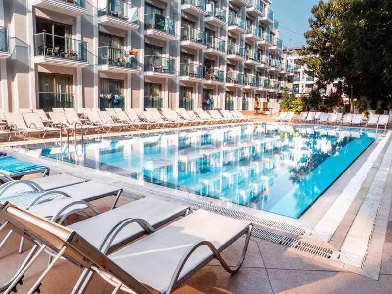Modern outdoor pool with sun loungers in front of a hotel building under clear sky.