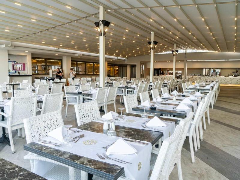 Large restaurant with many white tables and chairs, stylishly set and lit.