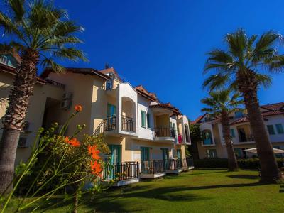 Mehrstöckige Wohngebäude mit Balkonen, umgeben von grünen Palmen und einem blauen Himmel.