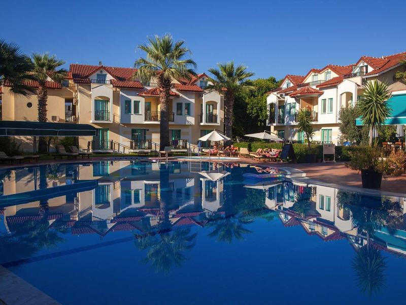 Hôtel avec grande piscine bleue, entouré de palmiers et de plusieurs bâtiments à deux étages.