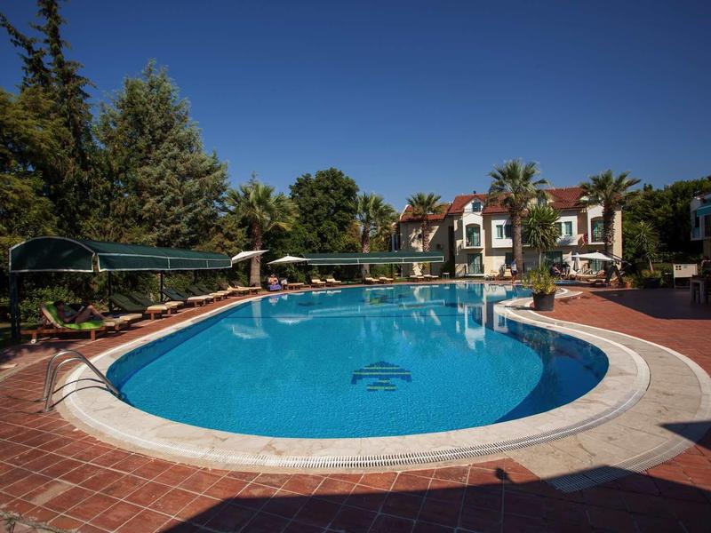 Piscine ronde avec eau bleu clair entourée de carreaux rouges et d'arbres dans un jardin d'hôtel.