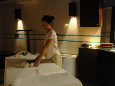 Une femme prépare une table de massage dans une salle de spa doucement éclairée.