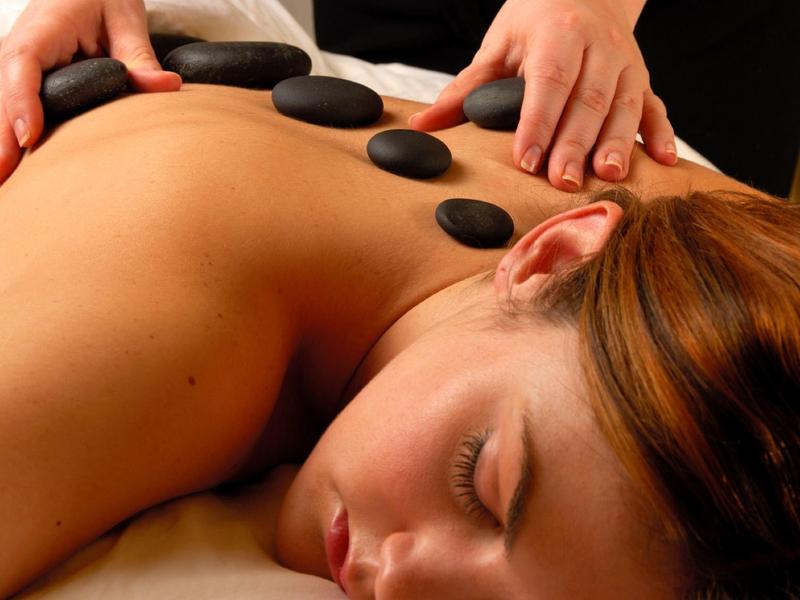 Femme recevant un massage aux pierres chaudes avec des pierres noires sur le dos dans un spa.