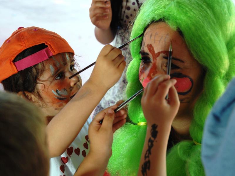 Enfant peignant le visage d'une personne portant une perruque verte éclatante avec des couleurs vives.