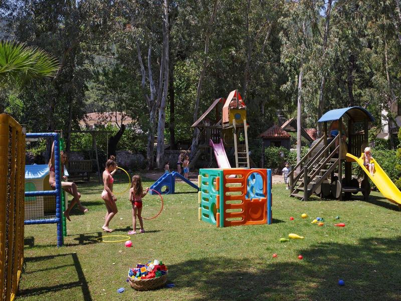 Aire de jeux avec équipements d'escalade, toboggans et enfants sur une pelouse verte sous des arbres.