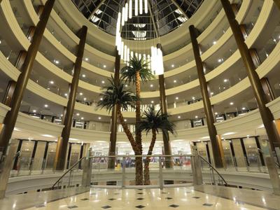 Innenansicht eines runden Atriums mit Glasdach, Palmen und mehrstöckigen Balkonen.