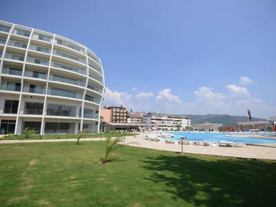 Modernes rundes Hotelgebäude mit Pool, Liegestühlen und Grünfläche unter blauem Himmel.