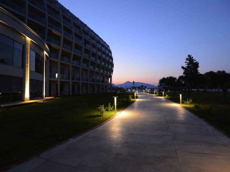 Beleuchteter Weg neben modernem Gebäude bei Abenddämmerung mit Bergen im Hintergrund.