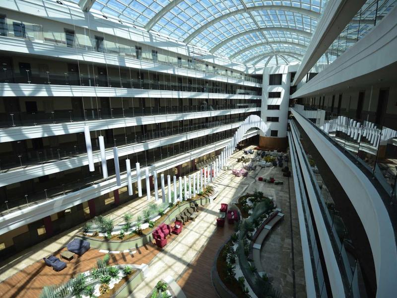 Großer heller Innenhof mit Glasdach, mehreren Stockwerken und dekorativen Pflanzen.