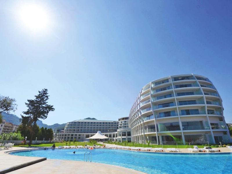 Moderner Hotelkomplex mit rundem Gebäude, Swimmingpool und klarem, blauem Himmel bei Sonnenschein.