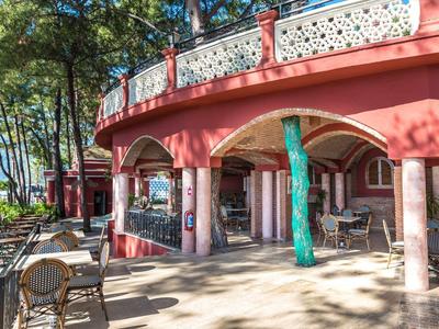 Restaurante abierto con arcos y columnas pintados de rojo junto a una orilla boscosa.