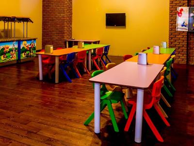 Sala de juegos colorida para niños con mesas pequeñas, sillas y juguetes con luz cálida.