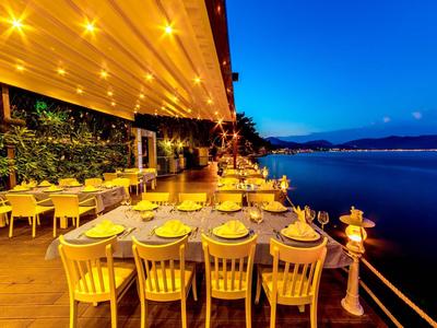 Terraza de restaurante junto al mar con mesas preparadas para cenar bajo luces cálidas al atardecer.