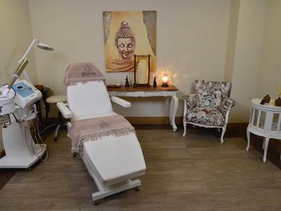 Stanza per trattamenti con sedia cosmetica, dispositivi, poltrona, tavolo e dipinto di Buddha sulla parete.