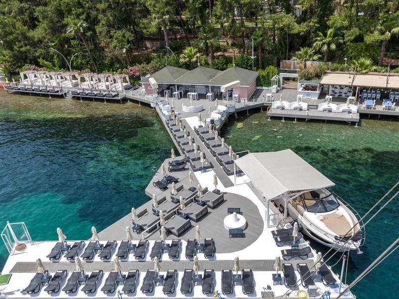 Vista aérea de un hotel con tumbonas y embarcadero para botes en agua clara.