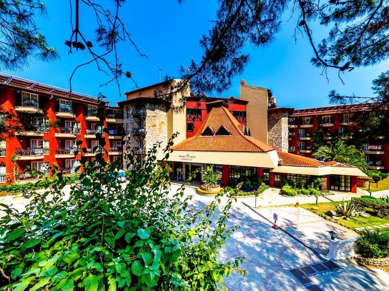 Gran edificio de hotel de varios pisos rodeado de árboles y áreas verdes bajo un cielo azul.