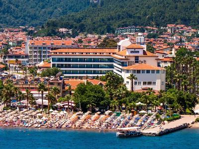 Hotel sulla riva con molti ombrelloni e vista su colline boschive sullo sfondo.