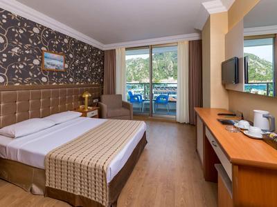 Hell eingerichtetes Hotelzimmer mit Doppelbett, Schreibtisch, Fernseher und Balkon mit Meerblick.