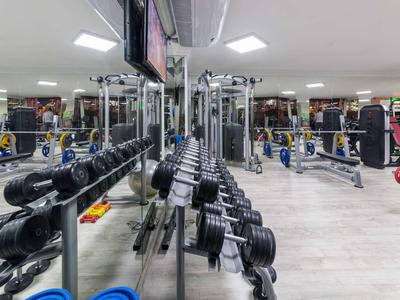 Dobře osvětlená posilovna s činkami, cvičebními stroji a zrcadlovou stěnou.