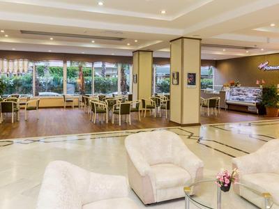 Hall dell'hotel luminosa con poltrone bianche, tavoli e un'area salotto con vista sul giardino.