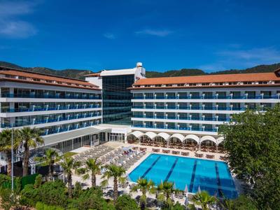 Moderní hotelová budova s velkým venkovním bazénem a palmami pod čistou oblohou.