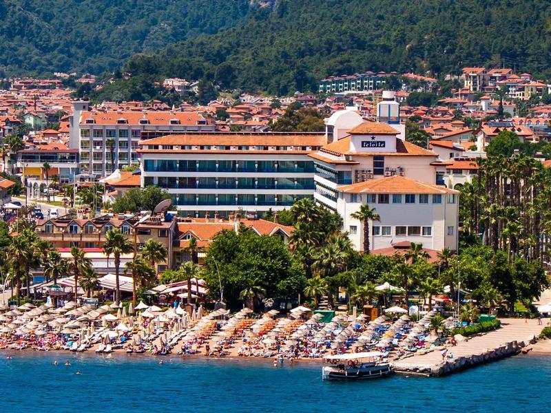 Hotel sulla riva con molti ombrelloni e vista su colline boschive sullo sfondo.
