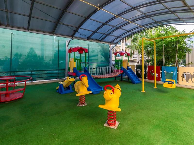 Area giochi coperta per bambini con scivoli, altalene e attrezzature colorate su pavimento verde.