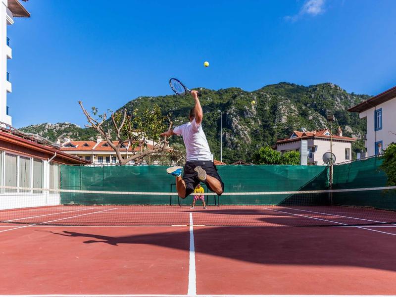 Persona che salta su un campo da tennis all'aperto tra le montagne.