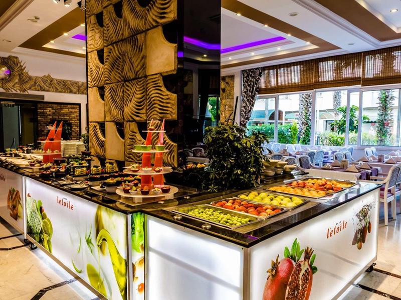 Isola buffet per la colazione moderna con frutta fresca e vari piatti in un ristorante luminoso.