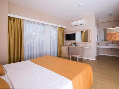 Modern eingerichtetes Schlafzimmer mit großem Bett, gelben Vorhängen, TV und einem Waschbeckenbereich.