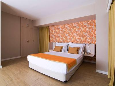 Jasno urządzony pokój hotelowy z podwójnym łóżkiem, pomarańczowym bieżnikiem i dekoracyjną ścianą.