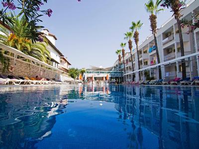 Großer Außenpool mit klarem blauem Wasser, umgeben von Palmen und modernen weißen Gebäuden.