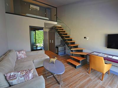 Wohnzimmer mit graßem Ecksofa, Holztreppe, orangem Sessel und Flachbildfernseher an der Wand.