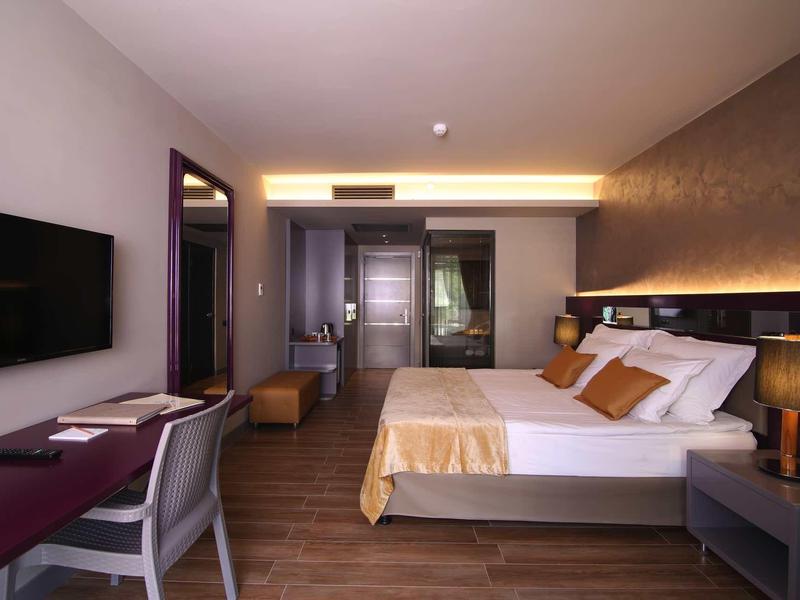 Modernes Hotelzimmer mit Doppelbett, Schreibtisch, Fernseher und warmem Licht.